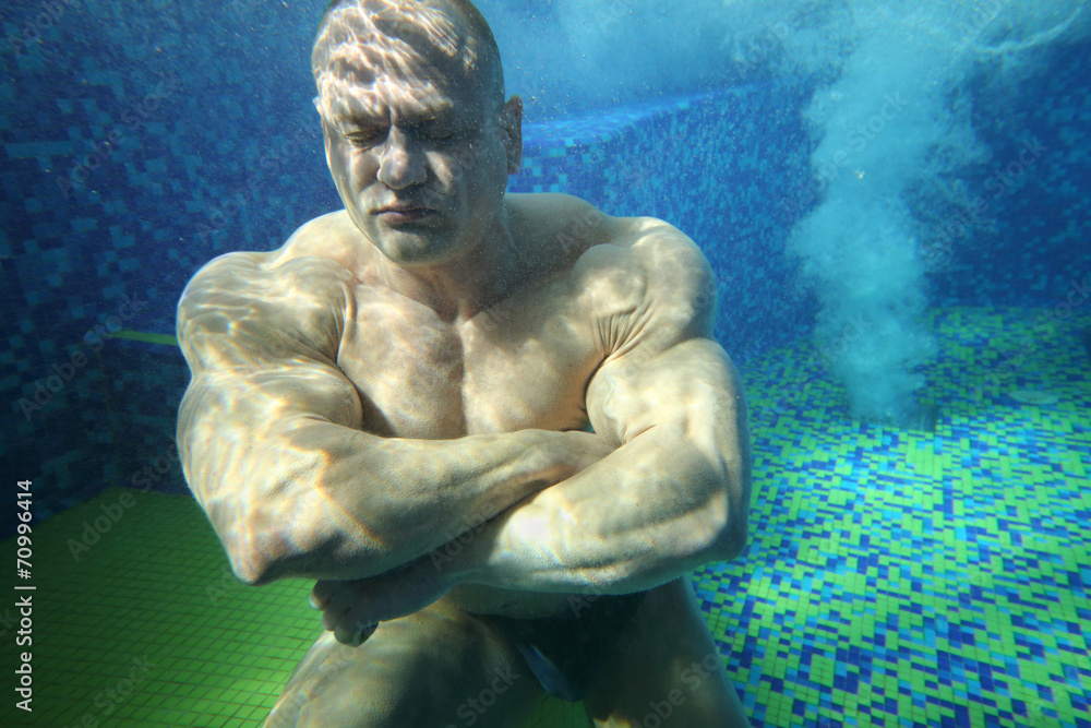 Bodybuilder with closed eyes on bottom of pool underwater Bodybuilder with closed eyes on bottom of pool underwater