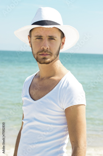 Man on beach looking to camera wearing hipster summer hat. © nenadmilosevic