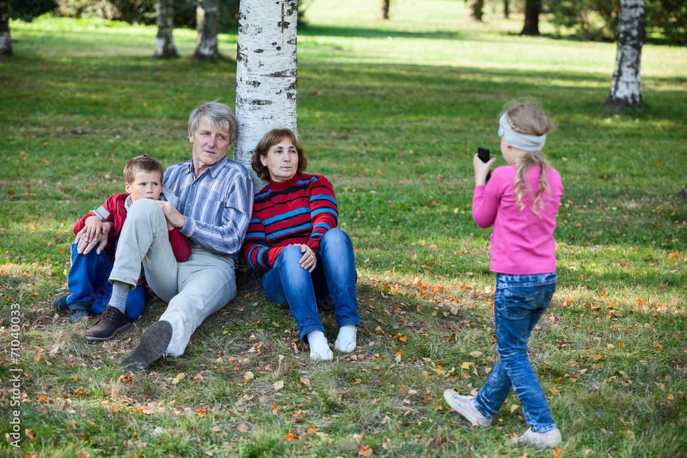 Family sitting under tree in park when girl makes picture phone