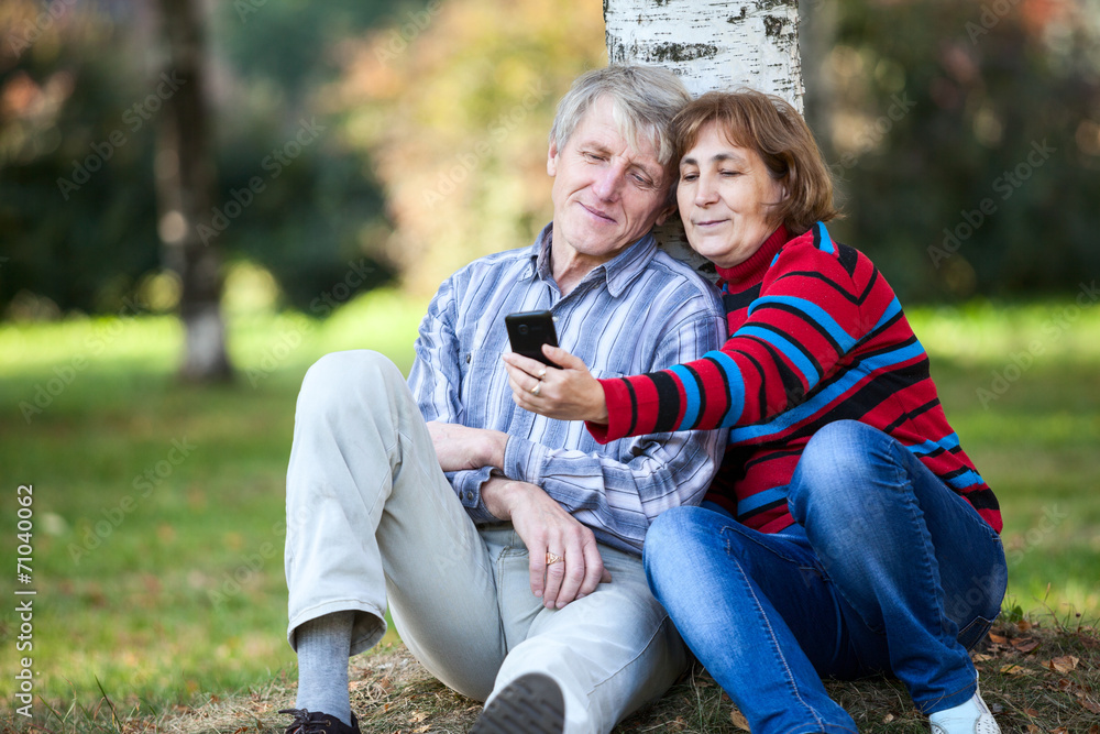 Mature couple sitting together and making selfie with phone park