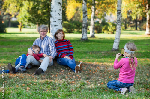Young pretty girl photographing her family by phone in park