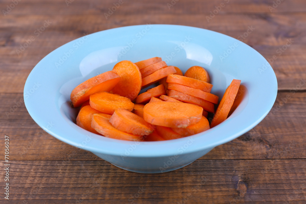 Slices of carrot in blue round bowl on wooden background Slices of carrot in blue round bowl on wooden background