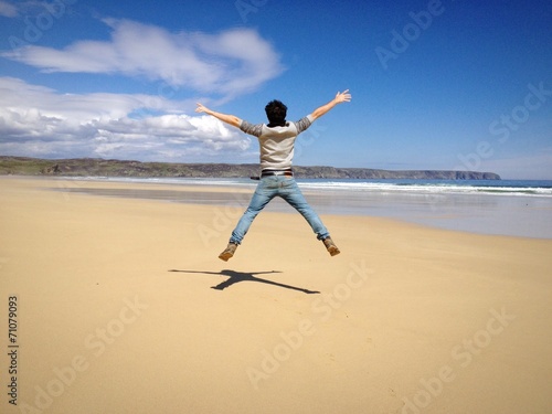 Young man form behind jumping in an empty beach