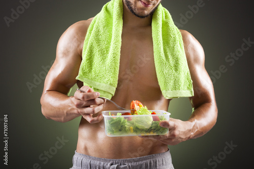 Fitness man holding a bowl of fresh salad on black background