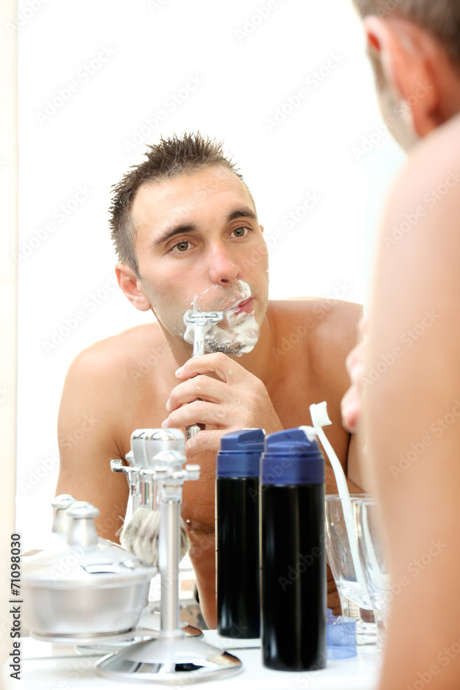 Young man shaving his beard in bathroom Young man shaving his beard in bathroom