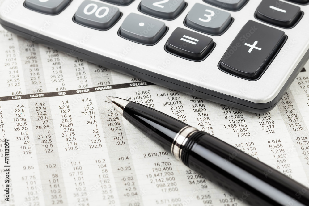 Pen, and calculator rest on stock price detail financial newspap Pen, and calculator rest on stock price detail financial newspap