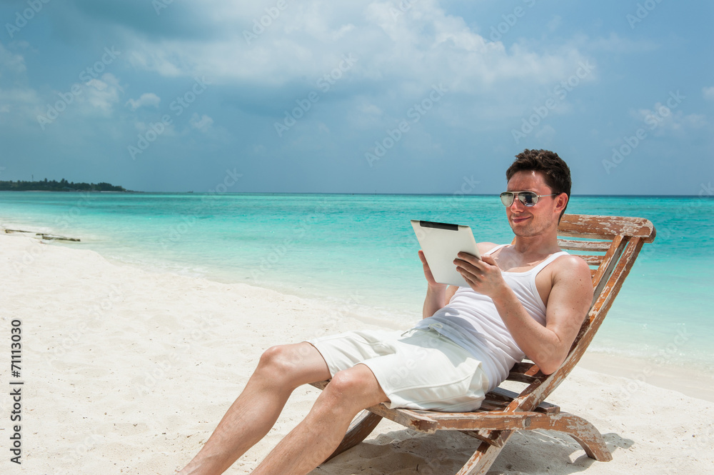 Man with tablet sitting on chair at the beach
