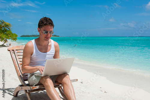 Man with sunglasses relaxing at the beach with laptop