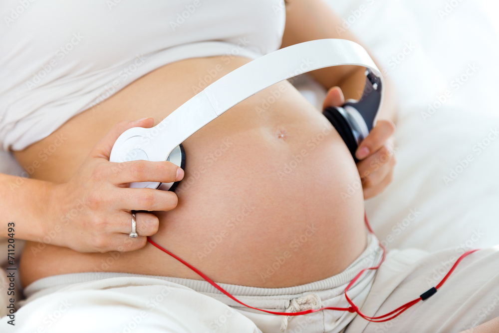 Pregnant woman putting headphones on her belly Stock Photo