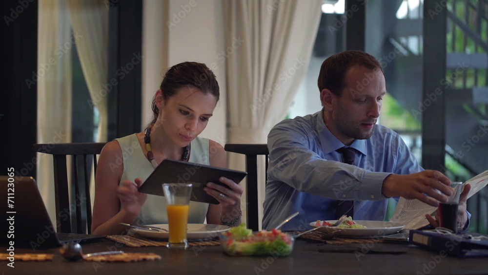 Business couple using tablet computer, reading newspaper and eat Business couple using tablet computer, reading newspaper and eat