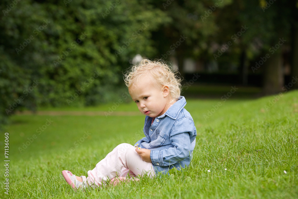Cute little girl sitting on green grass outdoors Cute little girl sitting on green grass outdoors