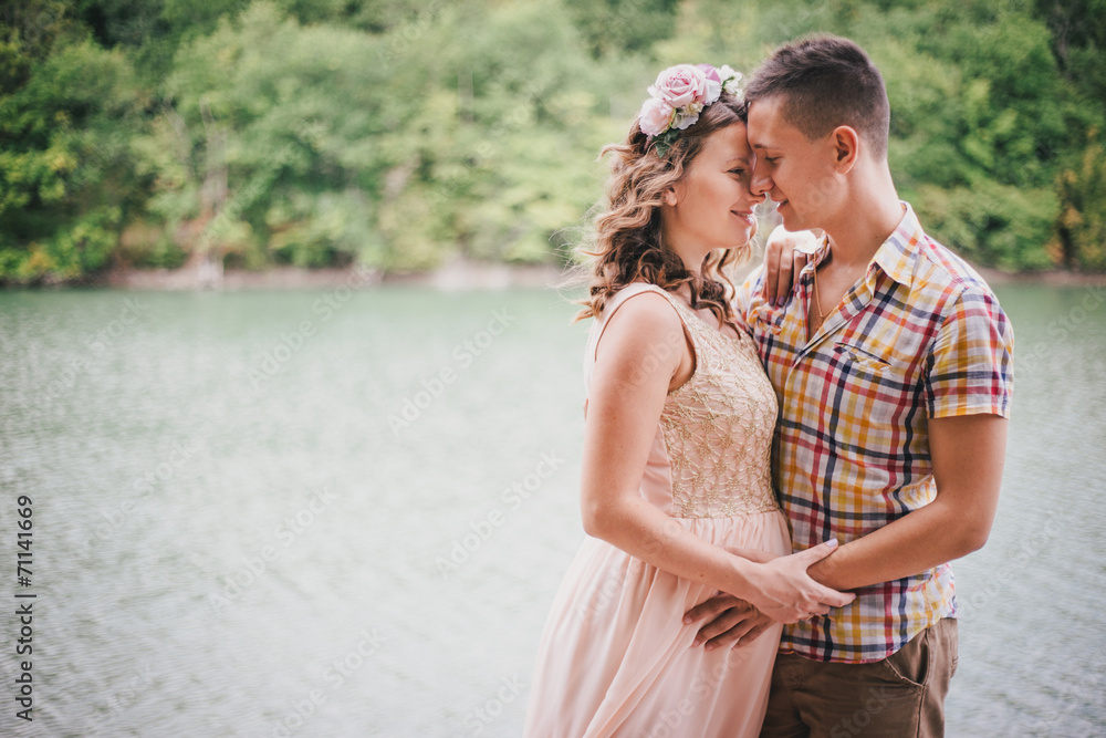 Young pregnant woman with her husband standing near lake