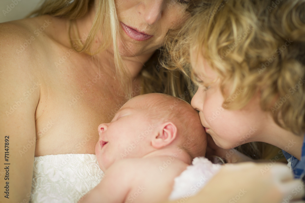 Young Mother Holds Newborn Baby Girl as Brother Kisses Her Young Mother Holds Newborn Baby Girl as Brother Kisses Her