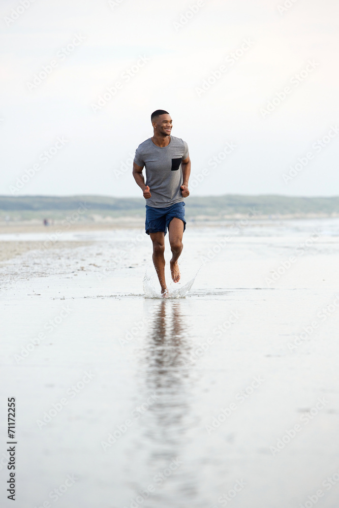 Man running barefoot on beach by water