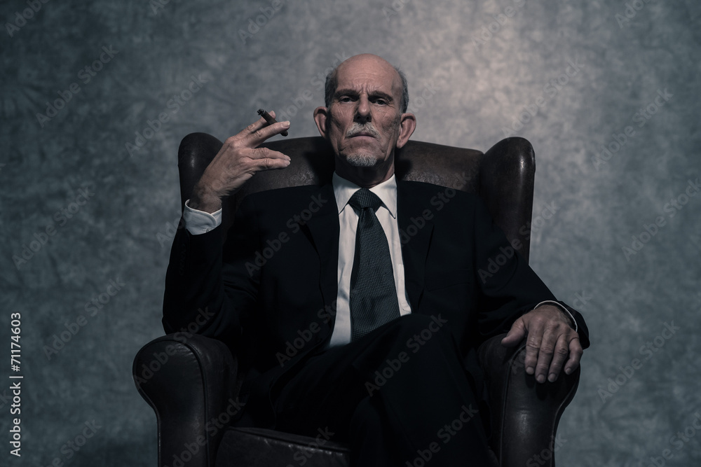 Cigar smoking senior businessman with gray beard wearing dark su Cigar smoking senior businessman with gray beard wearing dark su