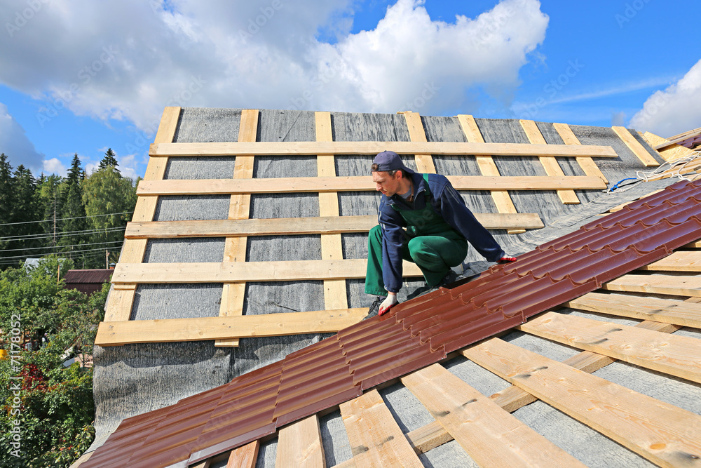 Worker puts the metal tiles on the roof of a wooden house Worker puts the metal tiles on the roof of a wooden house