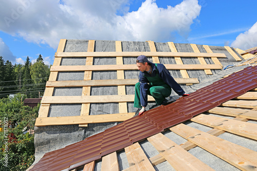 Worker puts the metal tiles on the roof of a wooden house