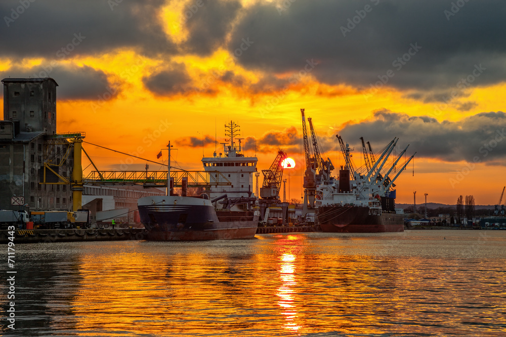 Ships and cranes with port warehouse at sunset.