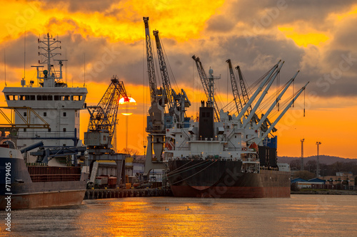 Ships and cranes with port warehouse at sunset.