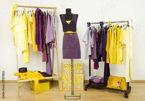 Wardrobe with violet and yellow clothes on hangers and mannequin