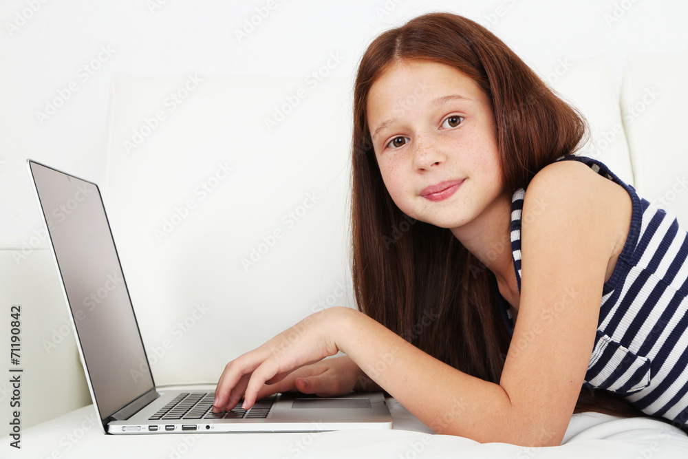 Beautiful little girl with laptop on sofa in room Beautiful little girl with laptop on sofa in room