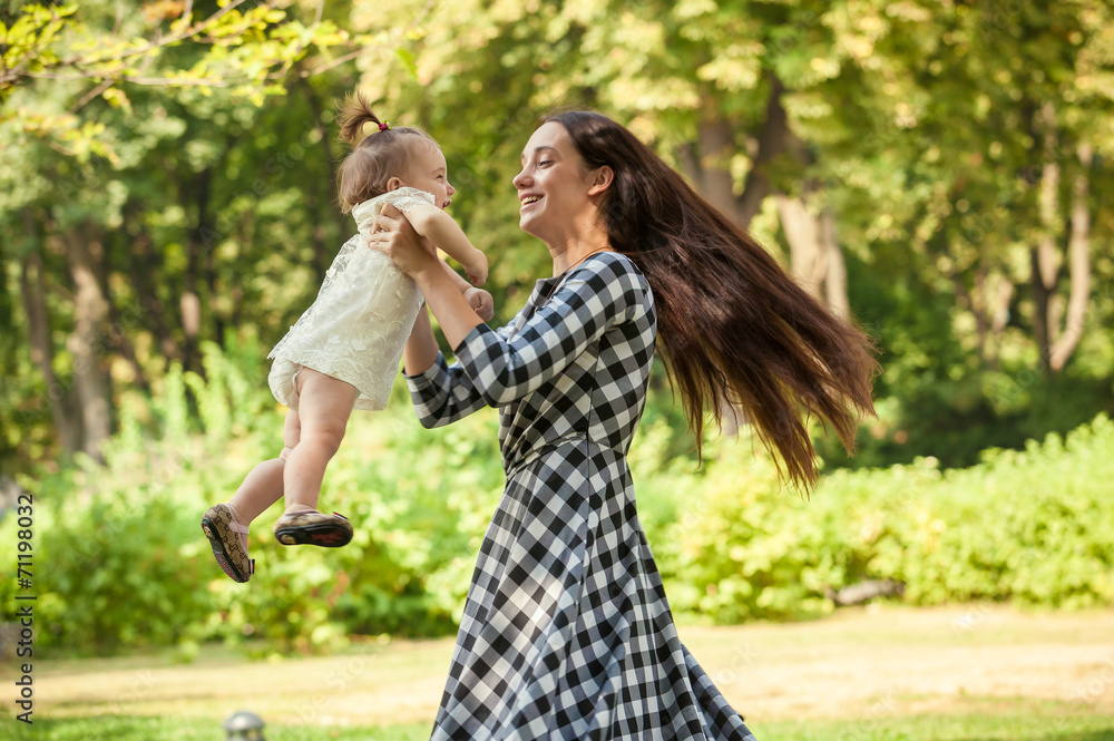 Fototapeta premium mother holding baby girl on hands and spinning around at park