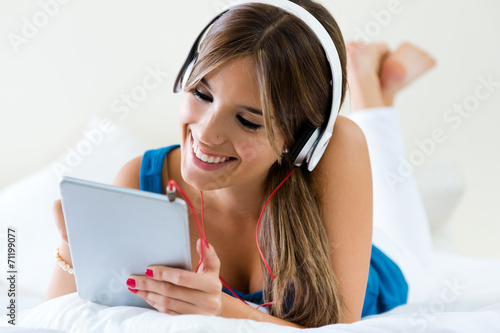 Beautiful girl listening to music with tablet on sofa at home.