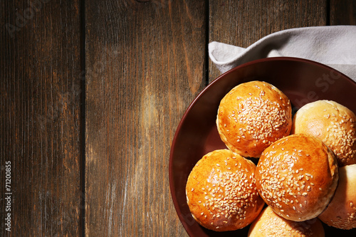 Tasty buns with sesame on plate, on wooden background