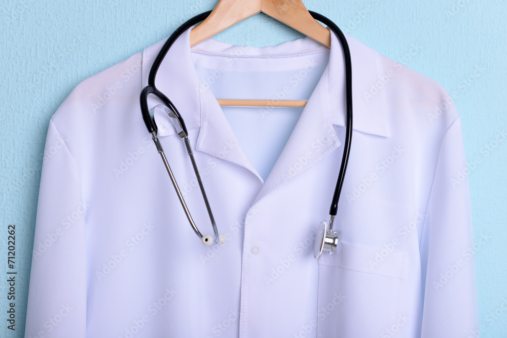 Doctor coat with stethoscope on hanger on blue background Doctor coat with stethoscope on hanger on blue background