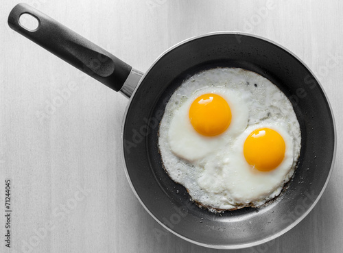 Vászonkép Two scrambled eggs in black frying pan on white wooden table