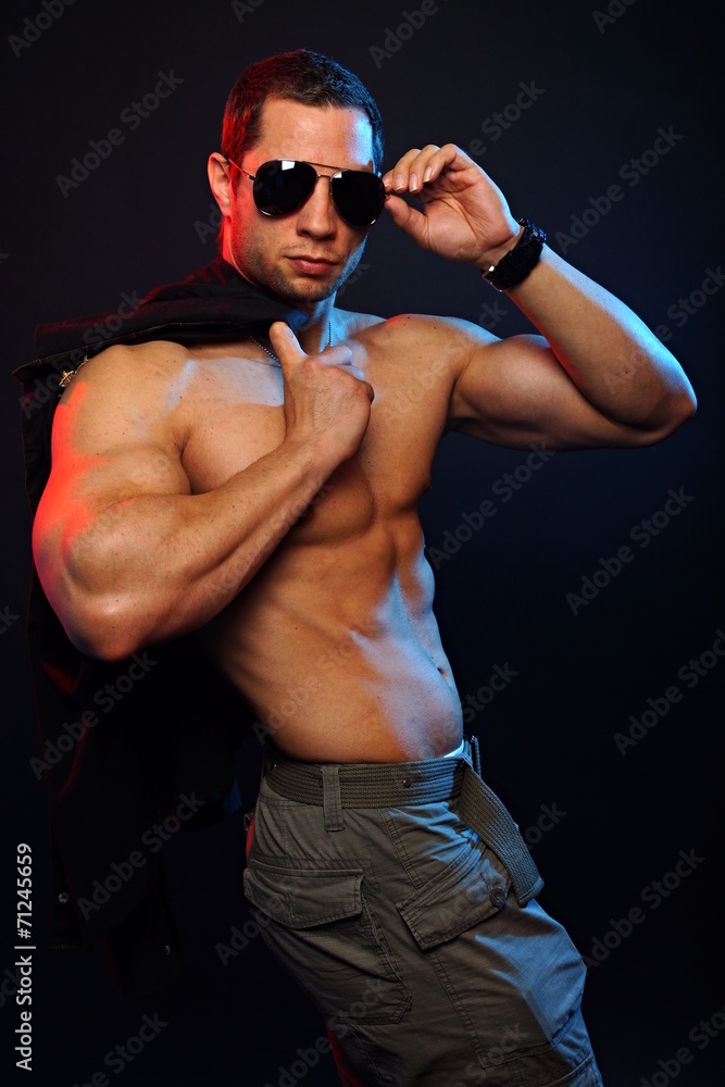 Muscular man in sunglasses posing with jacket over shoulder