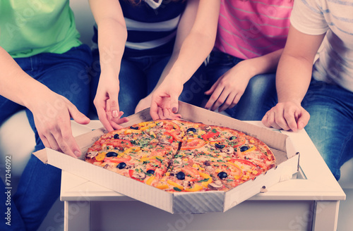 Group of young friends eating pizza in living-room on sofa