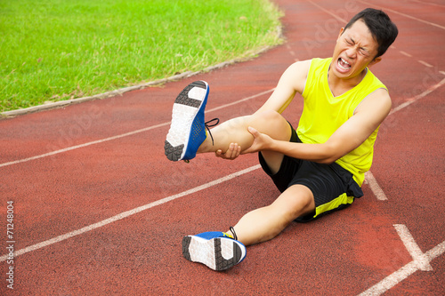 young male runner suffering from leg cramp on the track photo