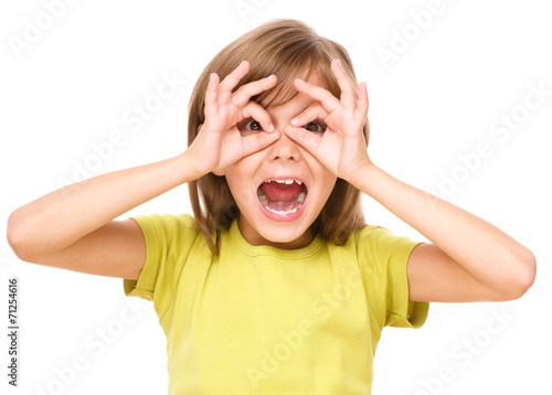 Fotografi Happy little girl is showing glasses gesture