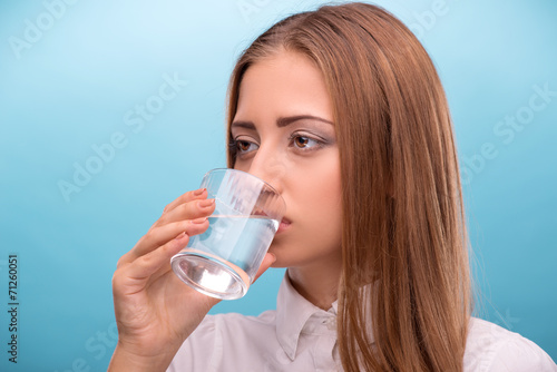 Portrait of young beautiful girl drinking clean water from a gla