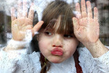 Novembertag: Portrait Mädchen klebt mit Gesicht und Händen an Fensterscheibe mit Regentropfen