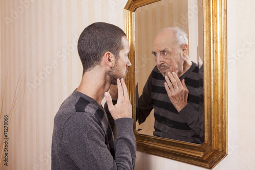 Fototapeta young man looking at an older himself in the mirror