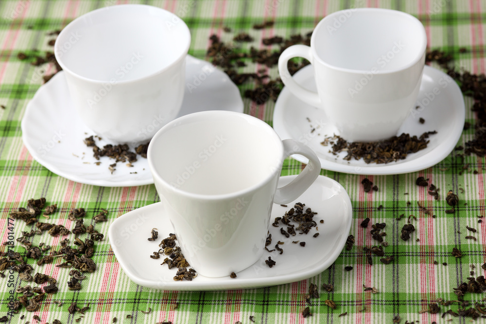 Three white empty cups and saucers with spilled green tea leaves Three white empty cups and saucers with spilled green tea leaves