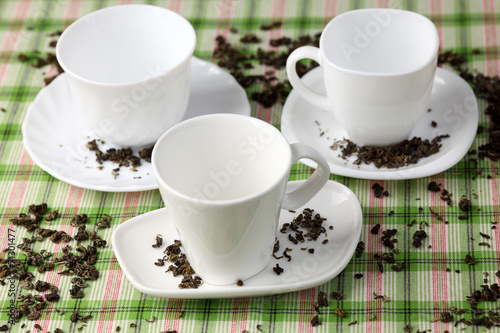 Three white empty cups and saucers with spilled green tea leaves