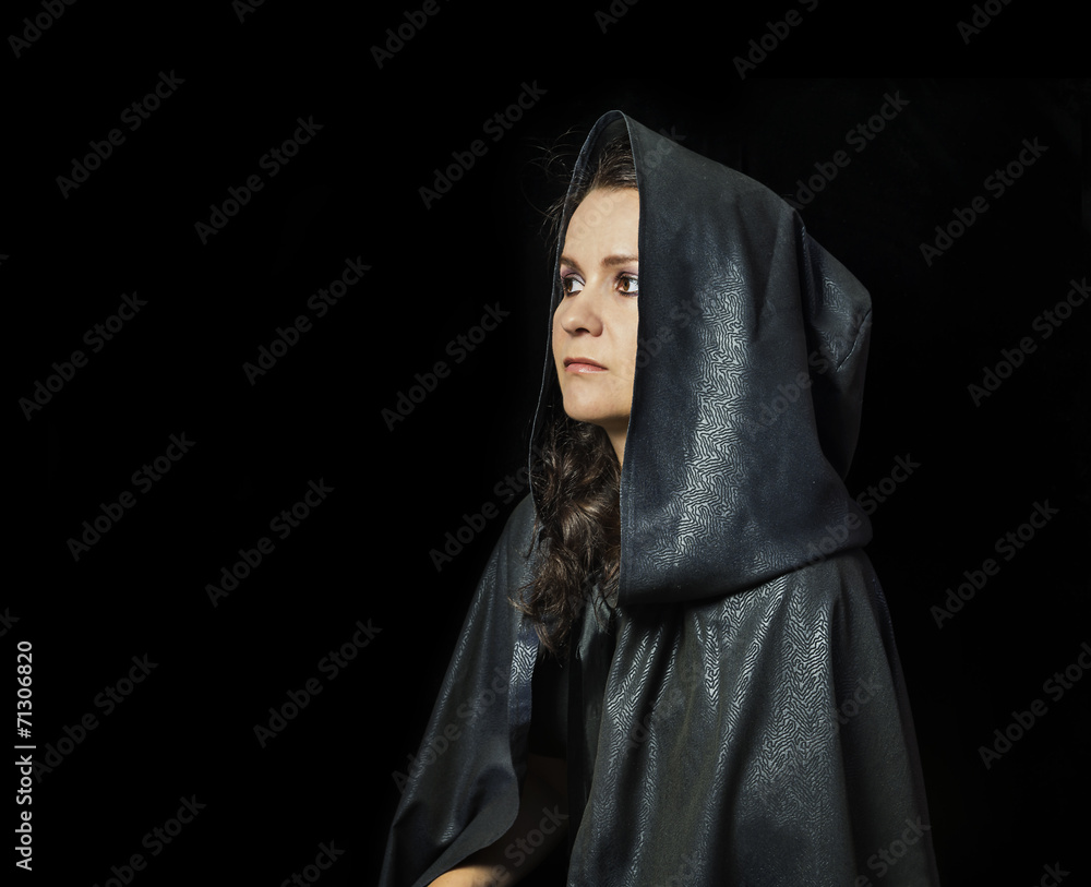 Thoughtful girl in black mantle on black background