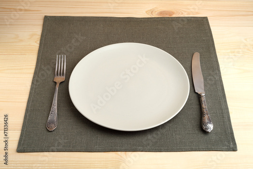 Empty plate with fork and knife on napkin on wooden table