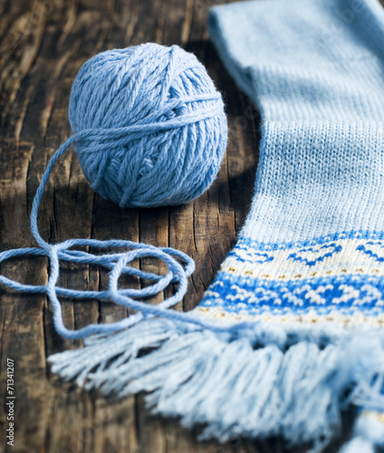 Ball of yarn and knitted scarf on wooden background