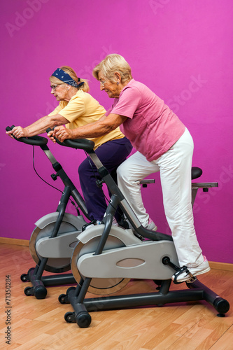 Two golden agers doing spinning in gym. photo