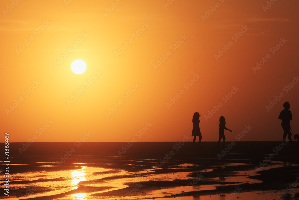 夕陽の海岸を散歩する親子のシルエット