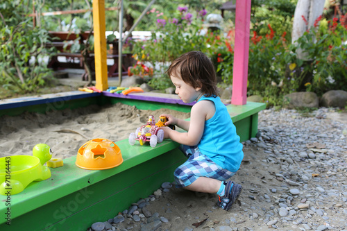 lovely boy playing with sand on playground in summer