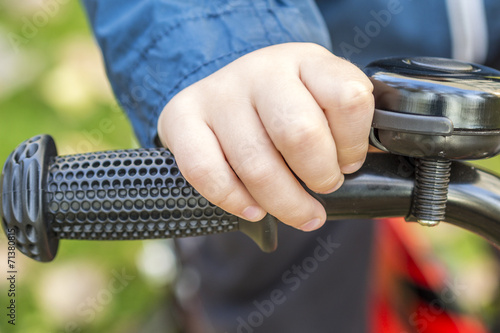 hand of a child on a handle with a bell of his bike