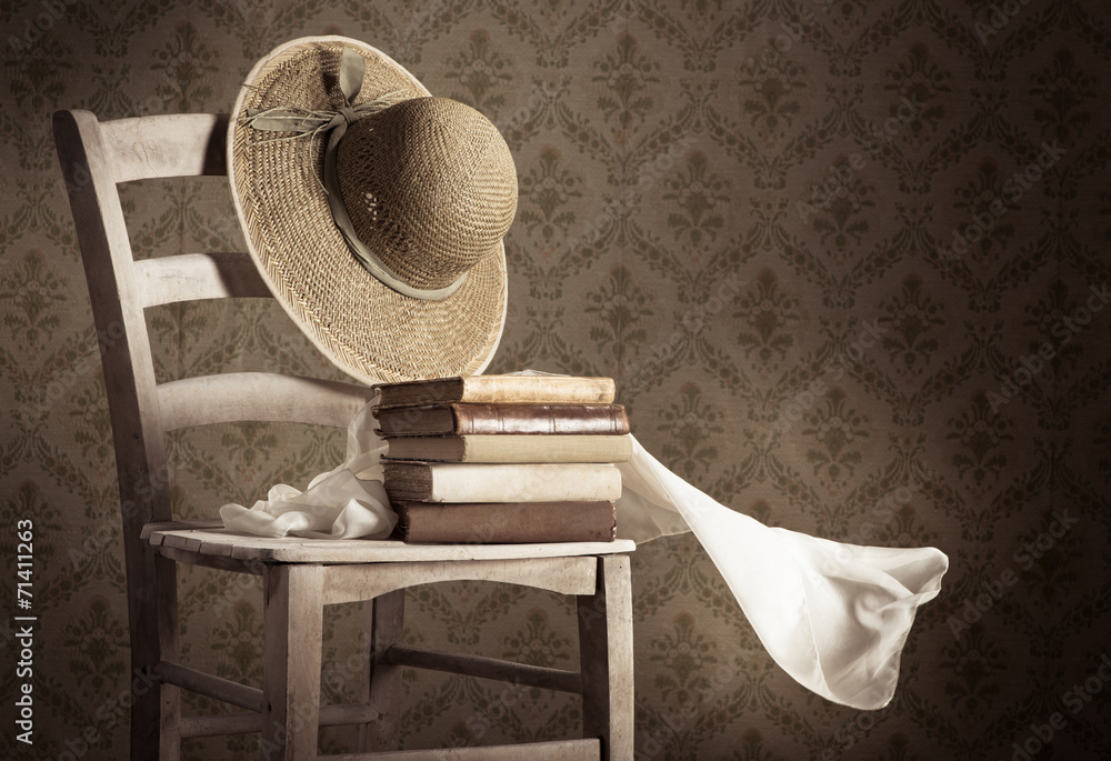 Naklejka premium Old books on a chair with straw hat