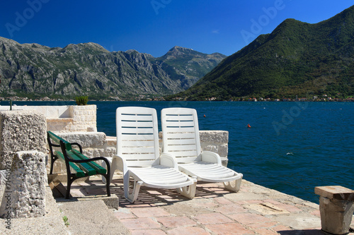 White plastic sunbeds on the shore of the Bay of Kotor