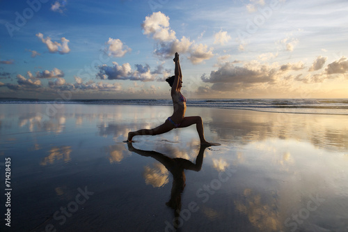 Young woman practicing yoga on the beach at sunset