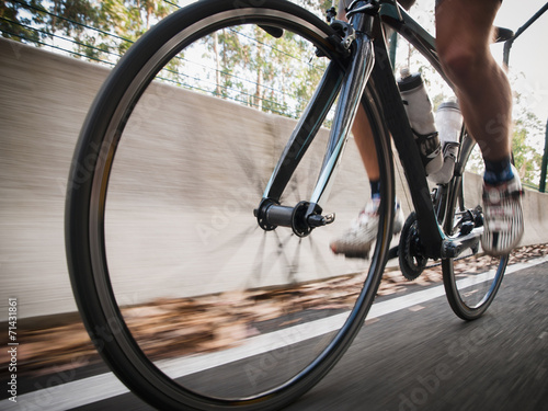 Detail of a road bike with a cyclist pedaling on a road.